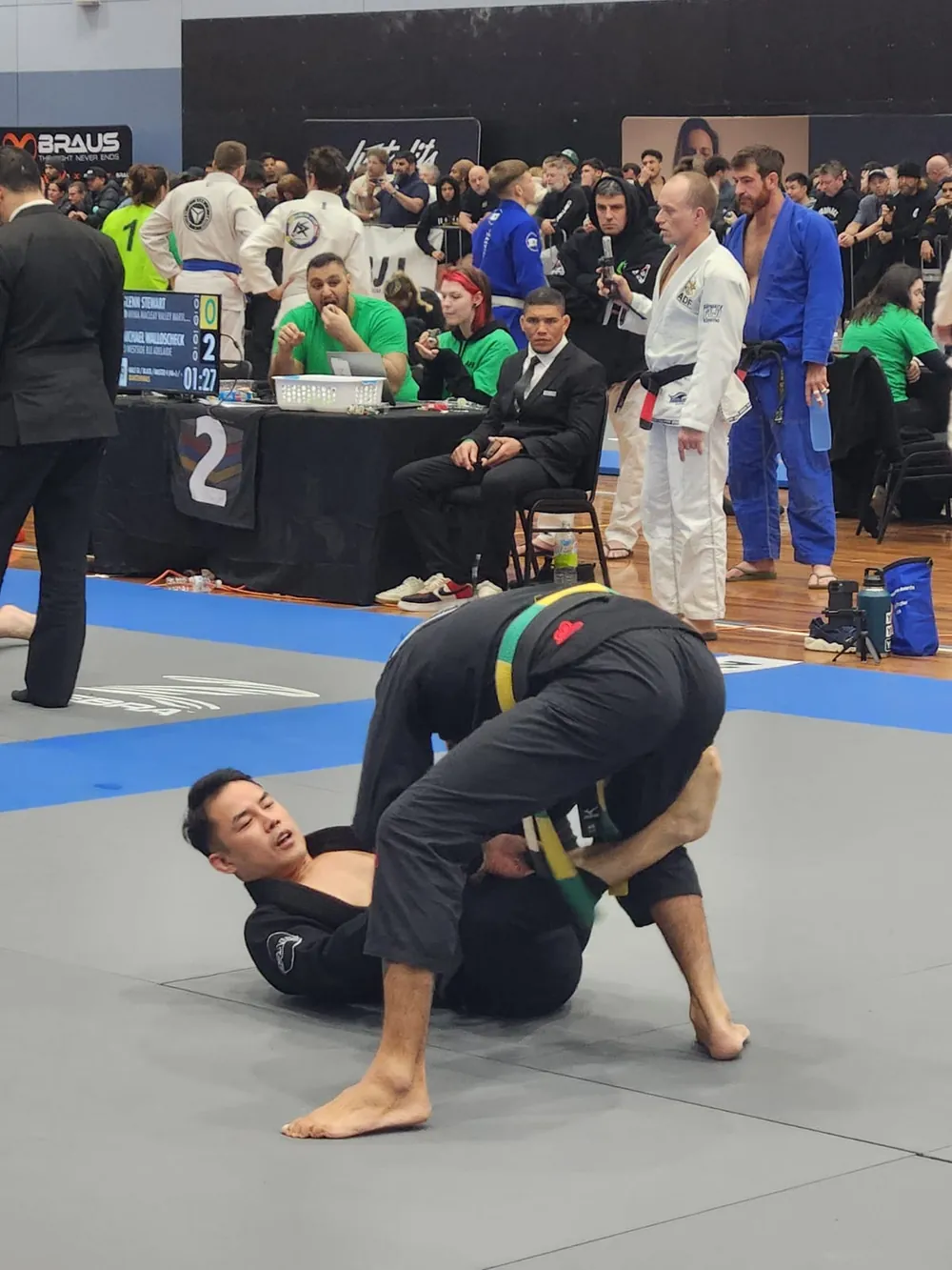 Two competitors rolling on the mat at a Brazilian Jiu Jitsu tournament