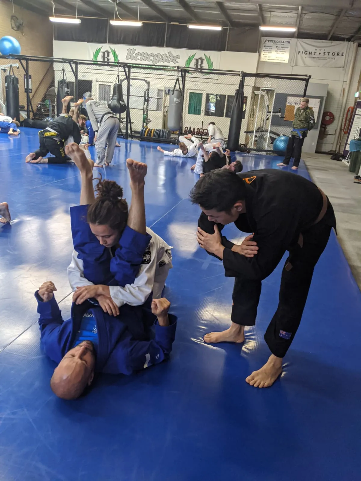 Jason Ng coaching two adults through a technique on the mat